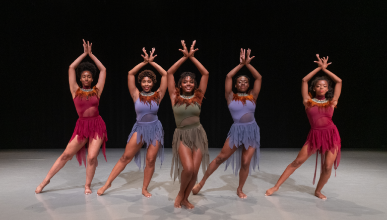 A group of five jazz dancers with their hands posed in the air.