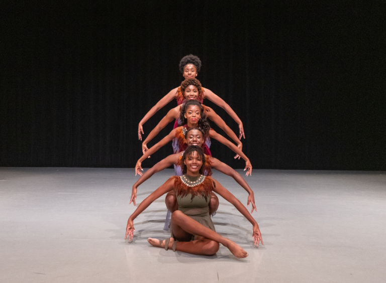 A group of five dancers posing on stage.