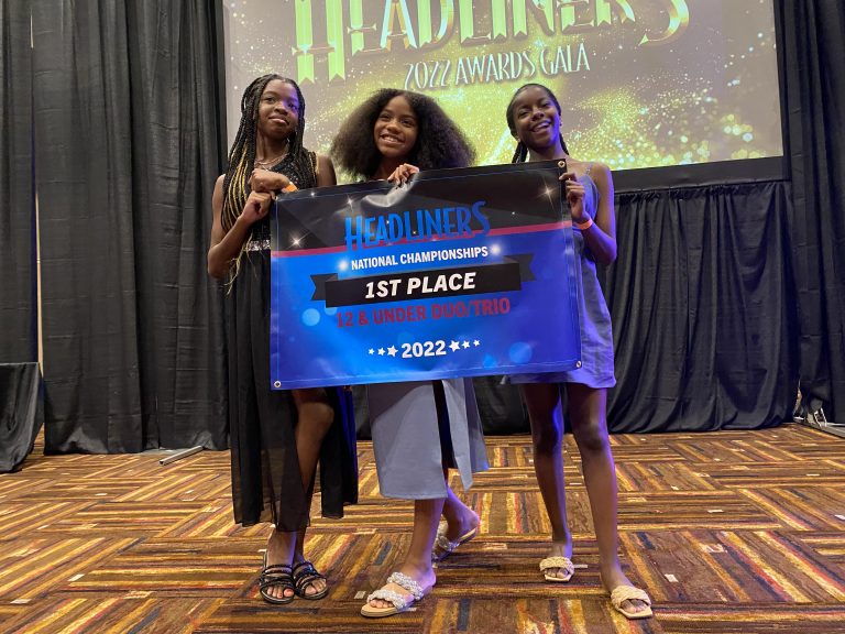 Three pre-teen dancers holding up a 1st Place sign with the word headliners on it.