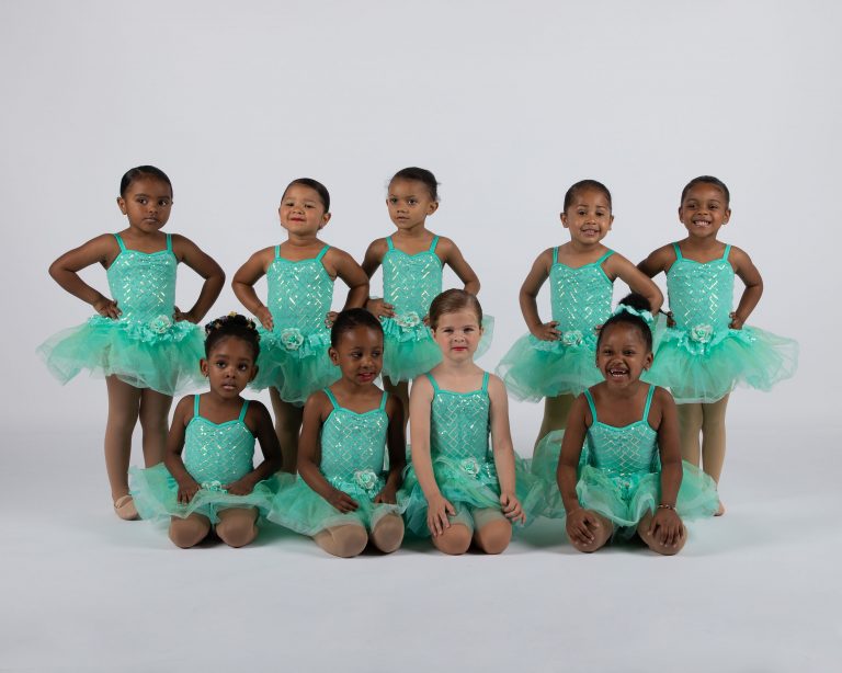 A group of young dancers in green tutus posing for a photo at a competitive dance event.
