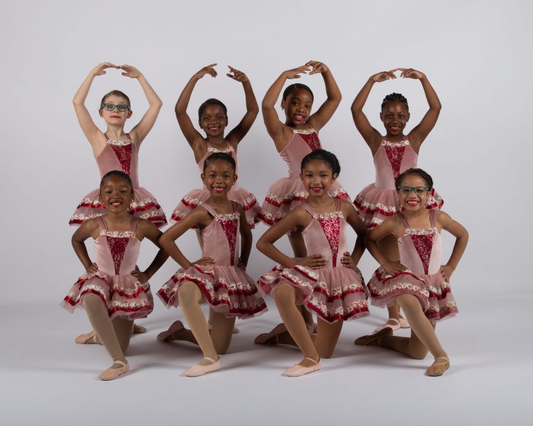 A group of pre-teen dancers posing for a photo in a ballet studio.