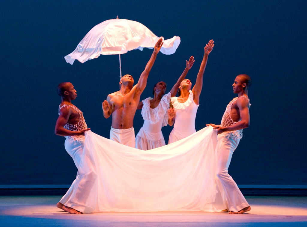 A group of dancers holding a white umbrella.