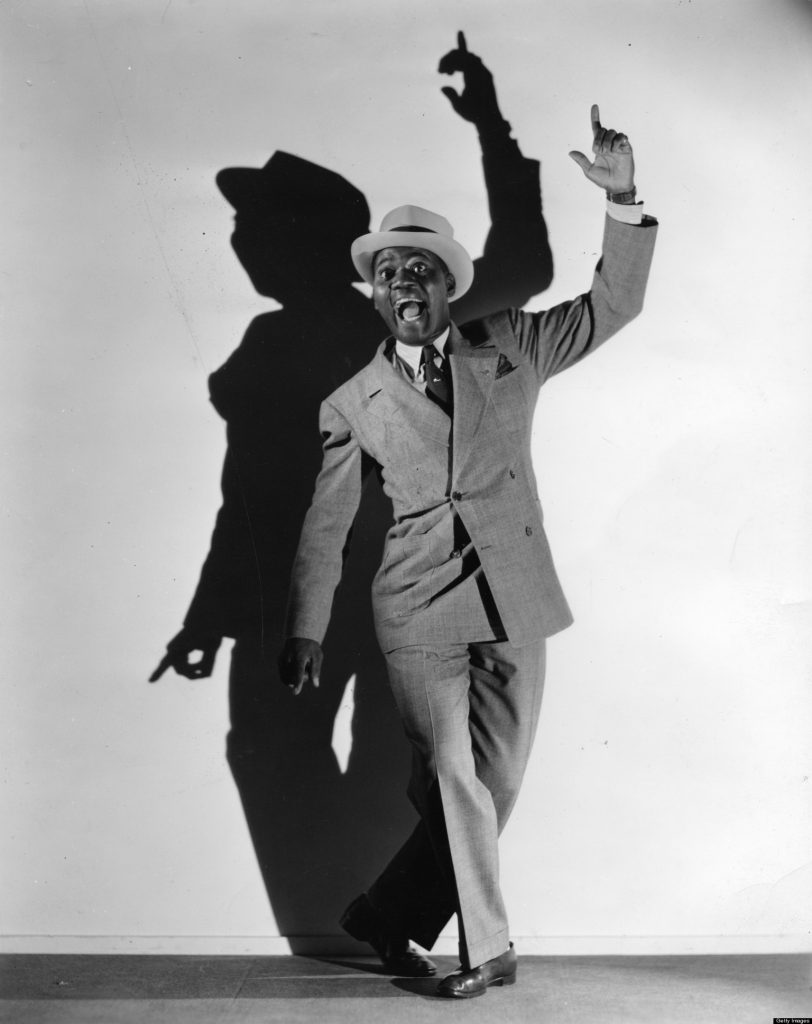 A black and white photo of a man in a suit and hat.